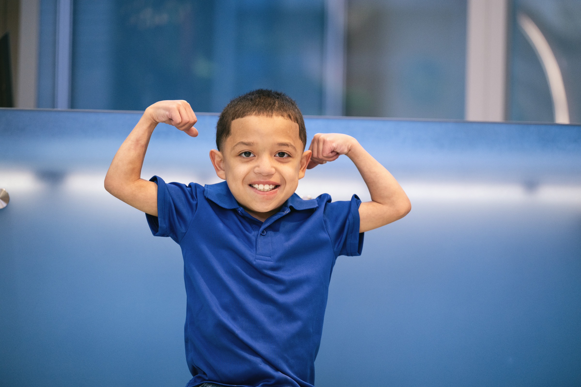 Young boy wearing blue shirt flexes his muscles for the camera
