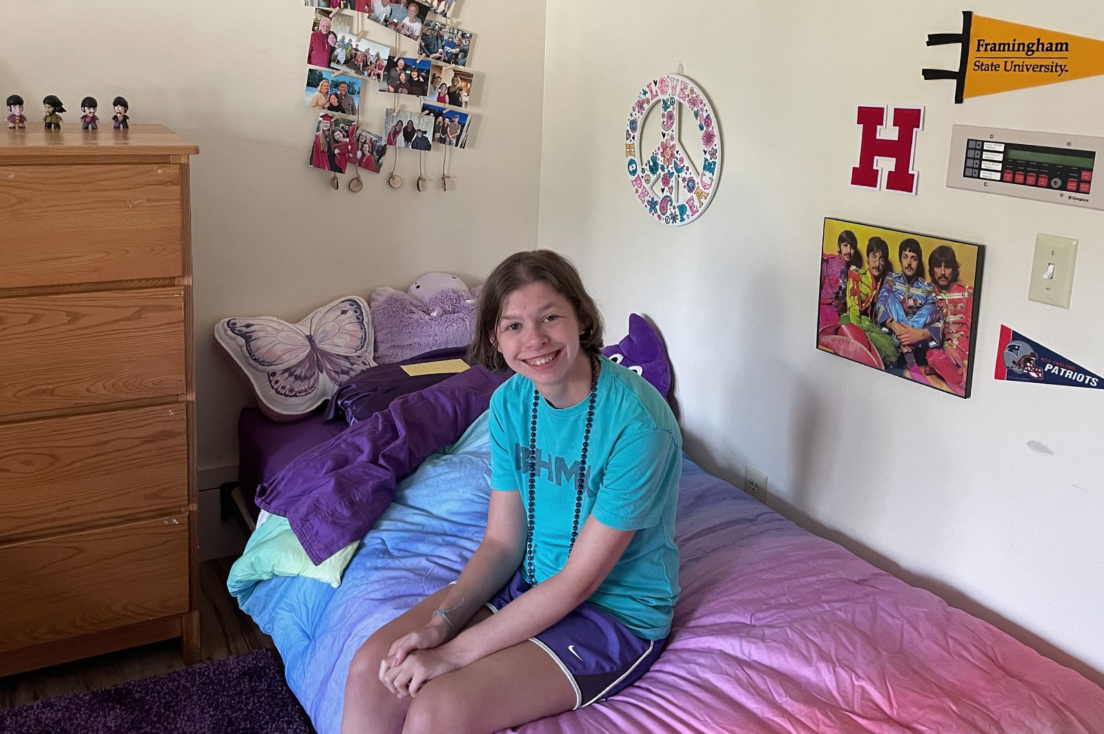 Teenage female in teal shirt sits on bed in college dorm room